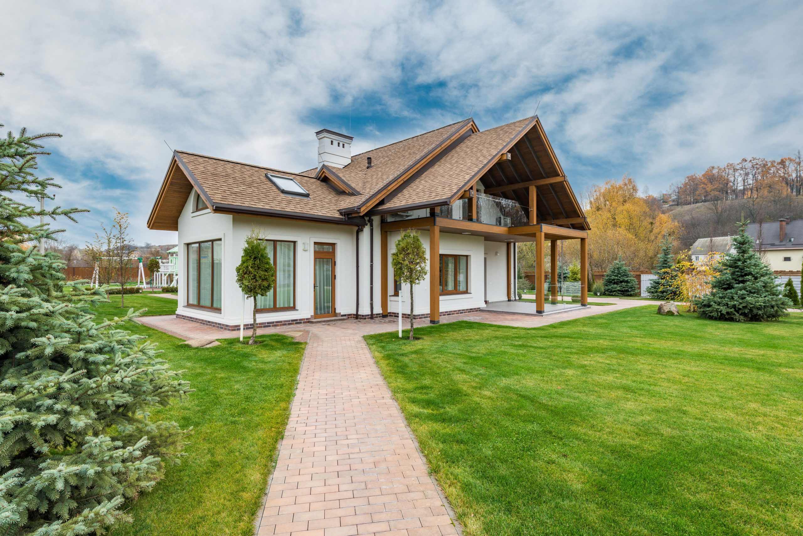 Exterior of small cottage house with green trees and grass in backyard under cloudy blue sky